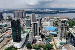 新山市区鸟瞰图，前景可见Menara JLand等高层商业建筑及在建项目，背景为柔佛海峡及对岸的新加坡，图片右下角带有theedgemalaysia水印